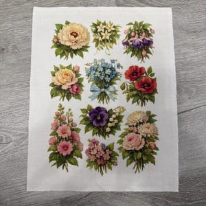 May include: A white fabric square featuring a collection of floral bouquets. The bouquets showcase a variety of flowers in shades of pink, red, blue, purple, and cream, with green foliage. The arrangements are printed on the fabric.