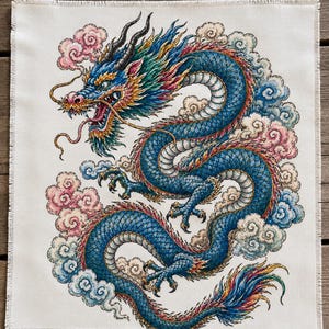 May include: A square fabric panel featuring a detailed illustration of a blue dragon with a long, winding body, sharp claws, and a multi-colored mane. The dragon is surrounded by stylized pink and blue clouds on a plain, off-white background.