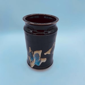 May include: A dark brown ceramic vase with a blue and gold abstract design. The vase has a rounded bottom and a slightly flared top.