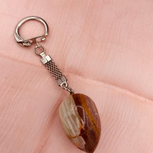 May include: A silver key chain with a brown and white agate stone charm. The stone is shaped like a teardrop and has a natural, organic look.