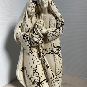 Puede incluir: Una figurita de cer&aacute;mica blanca de la Sagrada Familia. Las figuras est&aacute;n representadas de pie, con Mar&iacute;a sosteniendo al ni&ntilde;o Jes&uacute;s. La figurita est&aacute; decorada con esmalte craquelado negro.