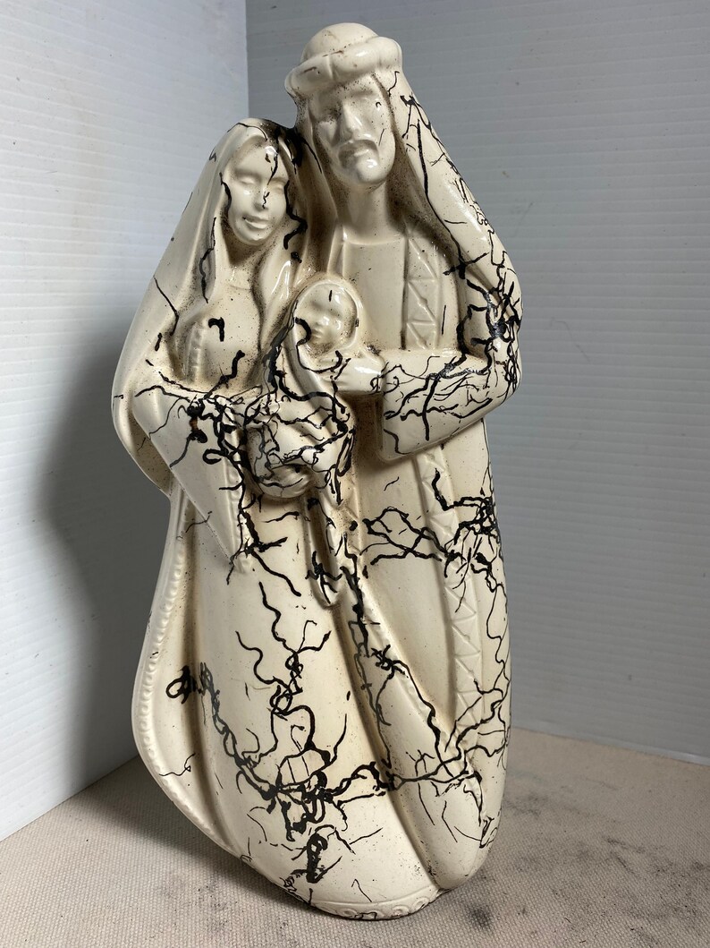 Puede incluir: Una figurita de cer&aacute;mica blanca de la Sagrada Familia. Las figuras est&aacute;n representadas de pie, con Mar&iacute;a sosteniendo al ni&ntilde;o Jes&uacute;s. La figurita est&aacute; decorada con esmalte craquelado negro.
