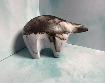 May include: A ceramic polar bear sculpture with a light gray body and a dark gray, textured head and back. The bear has a rounded body and a slightly elongated snout, standing on four short legs. The sculpture is a unique piece of art.