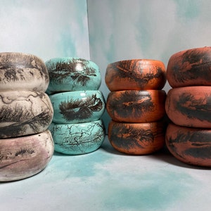 Puede incluir: Cuatro pilas de cuencos de cerámica con un diseño de plumas. Los cuencos son en tonos turquesa, marrón y blanco.