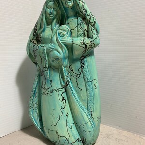 Puede incluir: Una figurita de cer&aacute;mica de la Sagrada Familia, que representa a Mar&iacute;a, Jos&eacute; y el ni&ntilde;o Jes&uacute;s. La figurita est&aacute; pintada en tonos azules y verdes con acentos negros. Las figuras est&aacute;n de pie juntas, con Mar&iacute;a sosteniendo al ni&ntilde;o Jes&uacute;s en sus brazos.