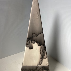 Può includere: Una piramide in ceramica bianca con segni neri. La piramide ha una base quadrata e una cima appuntita.