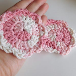May include: Two pink and white crocheted flower shapes with a scalloped edge.