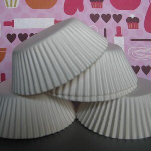 May include: Four white paper cupcake liners stacked on top of each other. The liners are fluted and have a smooth, white finish.