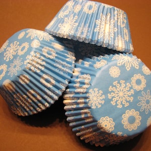 May include: A stack of blue cupcake cases with a white snowflake pattern.