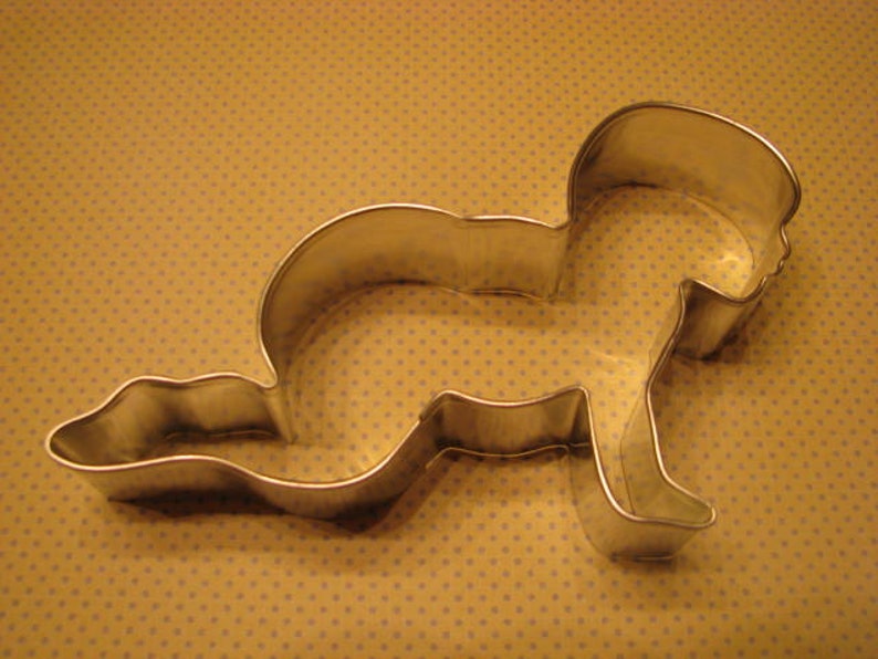 May include: A silver metal cookie cutter shaped like a baby lying on its stomach.