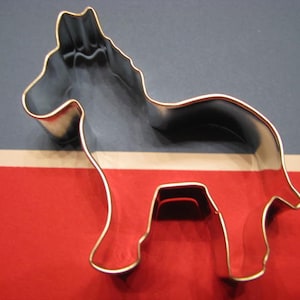 Peut inclure: Un emporte-pièce en métal argenté en forme d'âne. L'emporte-pièce est sur un fond rouge, blanc et bleu.