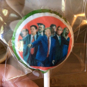 May include: A round lollipop with a white background and a red circle in the center. The circle features a group of men in suits and ties. The lollipop is wrapped in clear plastic.