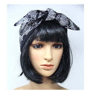 May include: Black headband with a white spiderweb pattern. The headband is tied in a bow on top of the head. The fabric is a dark color with a repeating web design.