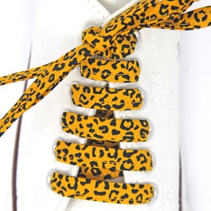 K&ouml;nnte beinhalten: Gelb-schwarze Schn&uuml;rsenkel mit Leopardenmuster, die an einem wei&szlig;en Paar Sneakers gebunden sind.