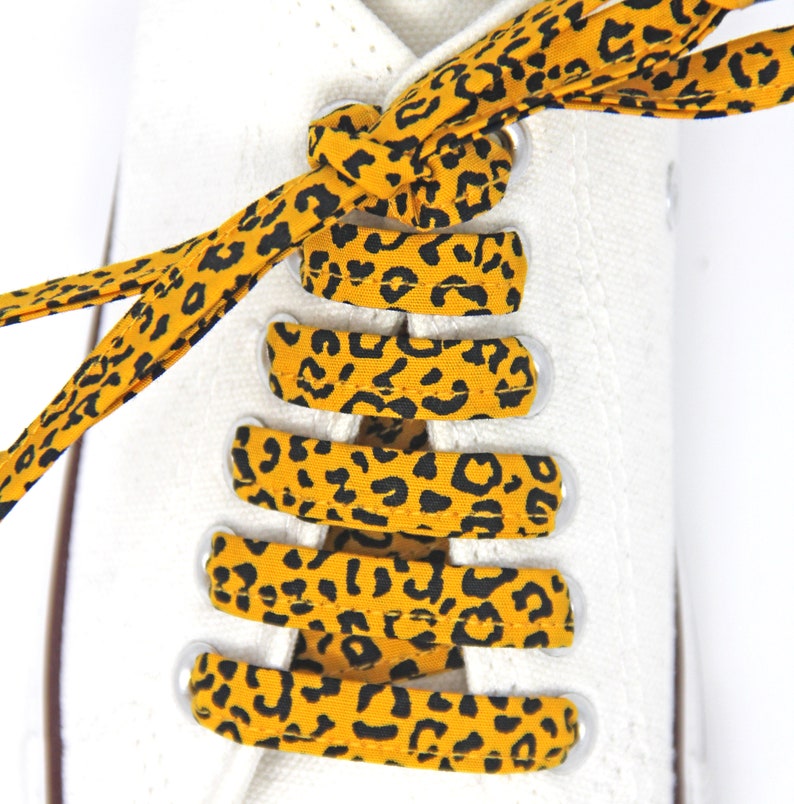 K&ouml;nnte beinhalten: Gelb-schwarze Schn&uuml;rsenkel mit Leopardenmuster, die an einem wei&szlig;en Paar Sneakers gebunden sind.