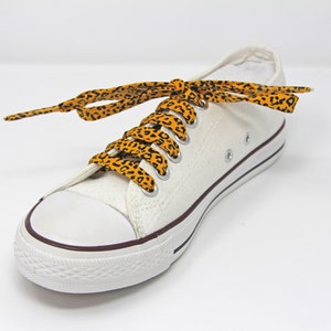 K&ouml;nnte beinhalten: Wei&szlig;e Canvas-Sneaker mit niedrigem Schaft und orangefarbenen und schwarzen Schn&uuml;rsenkeln mit Leopardenmuster.