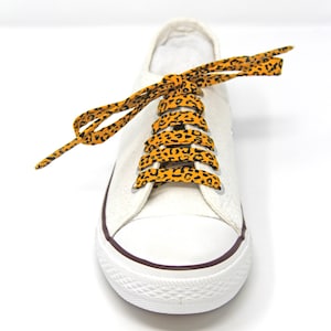 K&ouml;nnte beinhalten: Wei&szlig;e Canvas-Sneaker mit orangefarbenen und schwarzen Schn&uuml;rsenkeln im Leopardenmuster.