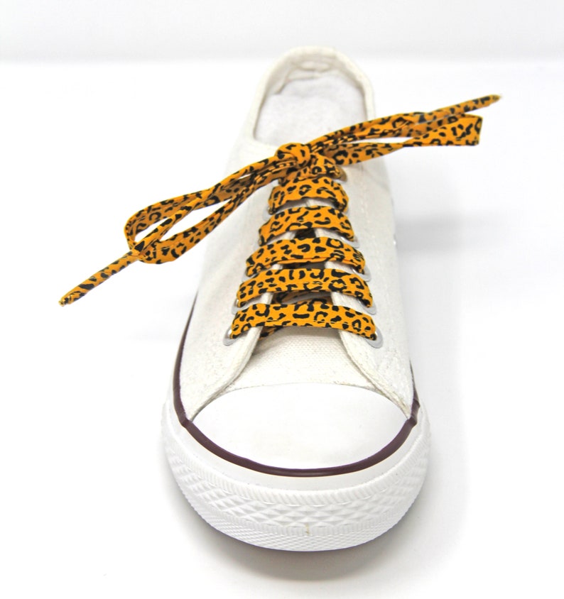 K&ouml;nnte beinhalten: Wei&szlig;e Canvas-Sneaker mit orangefarbenen und schwarzen Schn&uuml;rsenkeln im Leopardenmuster.