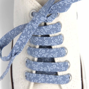 May include: White canvas shoes with blue patterned shoelaces tied in a criss-cross pattern.