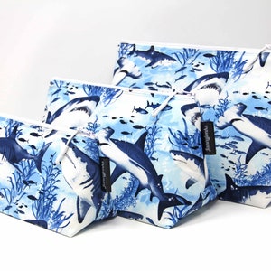 May include: Three blue and white zippered pouches with a shark and fish pattern. The pouches are made of fabric and have a white zipper. The largest pouch has the text "Junebug" printed on the side.