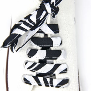 May include: White canvas shoes with black and white striped shoelaces tied in a bow. The shoelaces have a zebra print pattern.