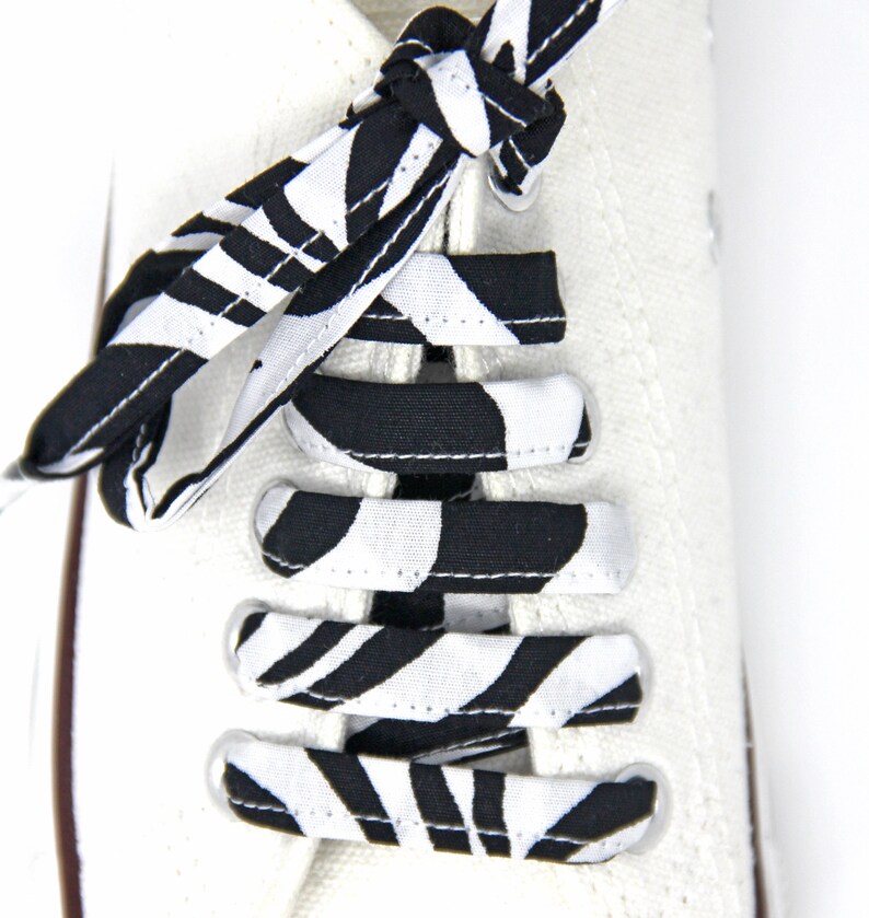 May include: White canvas shoes with black and white striped shoelaces tied in a bow. The shoelaces have a zebra print pattern.