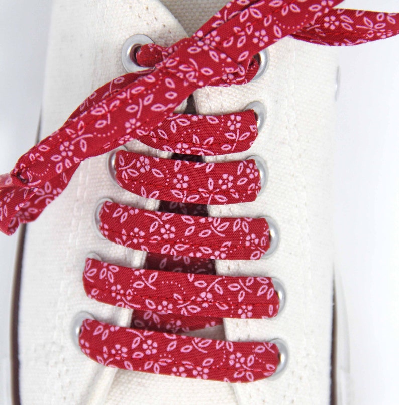 May include: Red and white patterned shoelaces are tied in a criss-cross pattern on a pair of white canvas shoes.