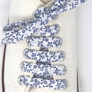 May include: White canvas shoes with blue and white patterned shoelaces. The shoelaces are tied in a bow at the top of the shoe.