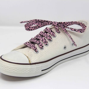 K&ouml;nnte beinhalten: Wei&szlig;e Canvas-Sneaker mit niedrigem Schaft und pinkfarbenen und schwarzen Schn&uuml;rsenkeln mit Leopardenmuster.