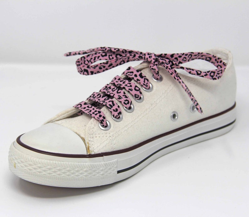 K&ouml;nnte beinhalten: Wei&szlig;e Canvas-Sneaker mit niedrigem Schaft und pinkfarbenen und schwarzen Schn&uuml;rsenkeln mit Leopardenmuster.