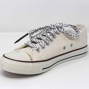 May include: White canvas low-top trainers with black musical note patterned laces.