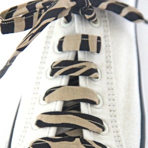 May include: White canvas shoes with black and tan zebra print shoelaces tied in a criss-cross pattern.