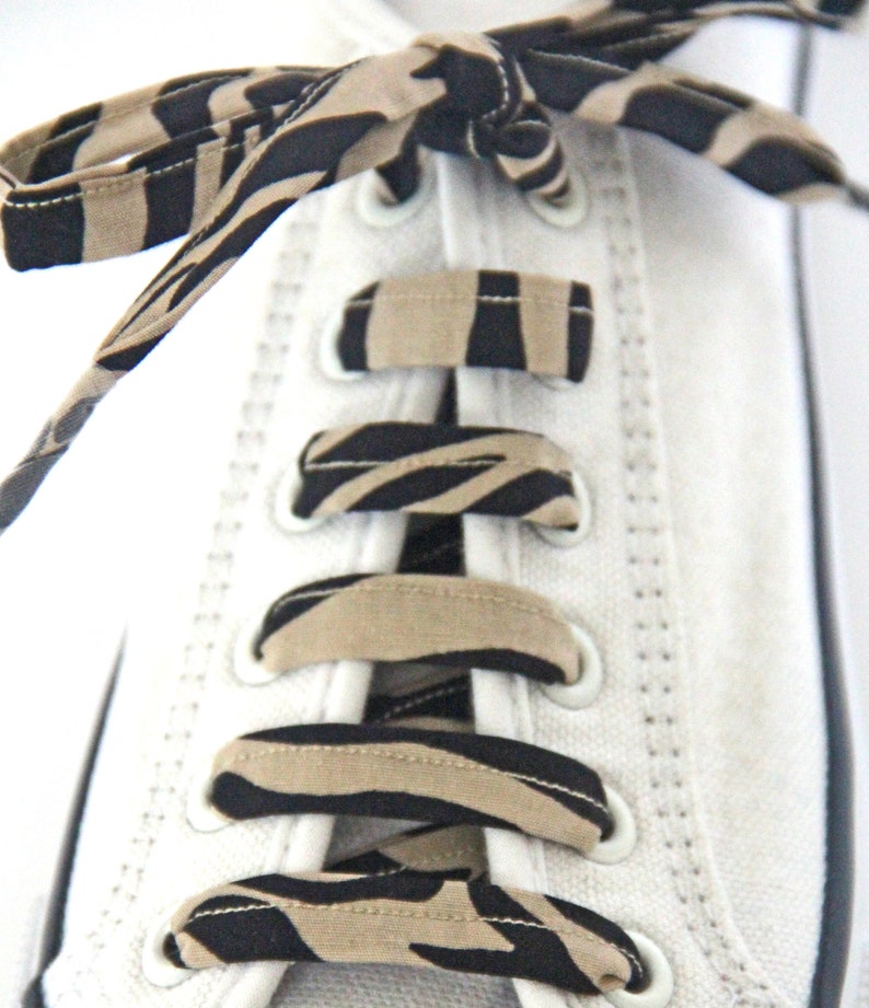 May include: White canvas shoes with black and tan zebra print shoelaces tied in a criss-cross pattern.