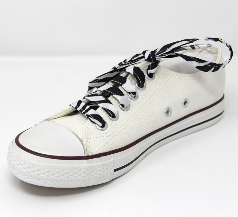 May include: White canvas low-top sneakers with black and white zebra print shoelaces.