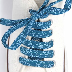 May include: White canvas shoes with teal blue shoelaces featuring a white floral pattern.