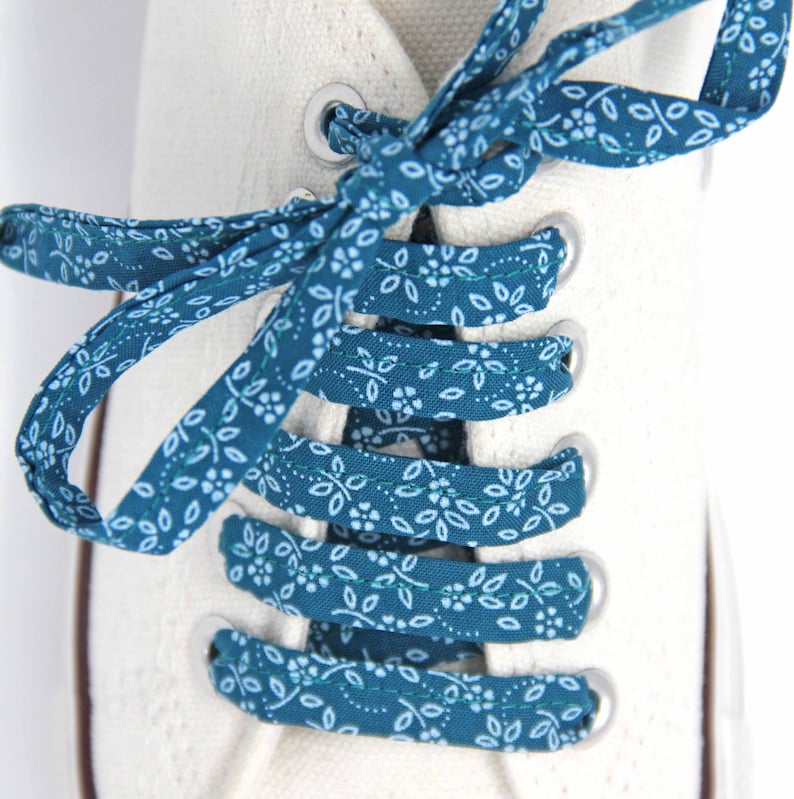 May include: White canvas shoes with teal blue shoelaces featuring a white floral pattern.