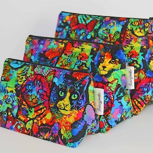 May include: Set of three colorful zippered pouches with a cat print design. The pouches are made of fabric and have a black zipper. The pouches are labeled "Janeyjonks".