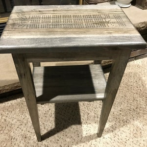 May include: A gray wooden end table with a shelf and a game board top. The game board has a pattern of holes.
