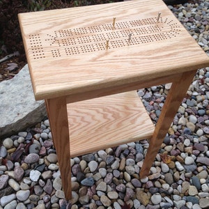 May include: A wooden game table with a peg board game surface and a lower shelf. The table is made of light wood and has a natural finish.