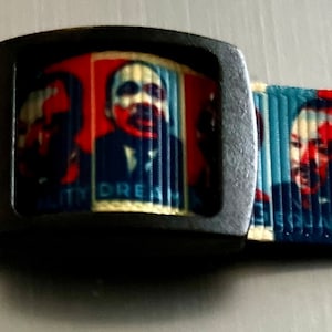 May include: A black and white patterned dog collar with a black plastic buckle. The collar features repeated images of Martin Luther King Jr. with the text "I Have A Dream" and "Equality" printed on the collar.