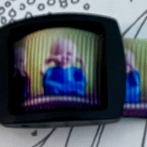 May include: A black and white dog collar with a repeating pattern of children covering their eyes, ears, and mouths. The collar has a black buckle.