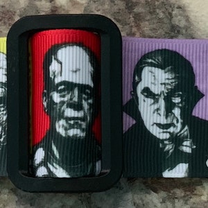 Puede incluir: Una cinta en blanco y negro con un patr&oacute;n repetido de caras de monstruos cl&aacute;sicos de pel&iacute;culas de terror. Las caras incluyen Frankenstein, Dr&aacute;cula, el Hombre Lobo y la Momia. La cinta est&aacute; sobre una superficie marr&oacute;n claro.