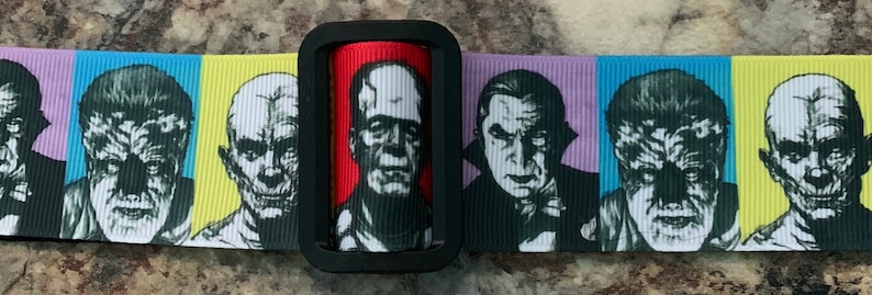 Puede incluir: Una cinta en blanco y negro con un patr&oacute;n repetido de caras de monstruos cl&aacute;sicos de pel&iacute;culas de terror. Las caras incluyen Frankenstein, Dr&aacute;cula, el Hombre Lobo y la Momia. La cinta est&aacute; sobre una superficie marr&oacute;n claro.
