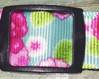May include: A floral patterned dog collar with a black plastic buckle. The collar features a light blue background with pink and white flowers and green leaves. The collar is approximately 1 inch wide.