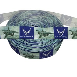 May include: A roll of ribbon featuring a repeating pattern of U.S. Air Force logos and fighter jets. The ribbon has a blue and white camouflage design. The text "U.S. AIR FORCE" is printed on the ribbon.