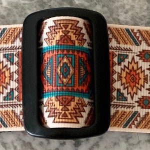 May include: A white guitar strap with a black buckle and a colorful geometric pattern in shades of orange, brown, blue, and turquoise.