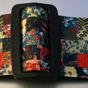 May include: A colorful guitar strap with a patchwork design featuring various patterns and colors. The strap has a black adjustable buckle.