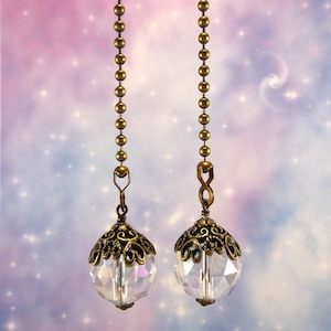 May include: Two antique brass ceiling fan pull chains with clear crystal ball ends. The chains have a decorative, ornate design.