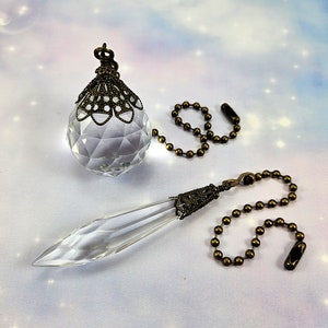 May include: Two crystal ceiling fan pulls with ornate metal accents and brass chains. The crystal pulls are clear and have a faceted design.