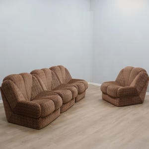 Può includere: Un set di divani marrone a fantasia, composto da un divano a tre posti e una poltrona abbinata. L'arredamento presenta un design arrotondato e strutturato, collocato in una stanza con pareti e pavimenti chiari.